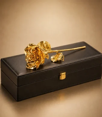 24K Gold-Dipped Rose by GoldPrivé resting on a black leather box beside the emblem, bloom, leaves and stem all in gold