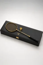 24K Gold Badminton Set by GoldPrivé lying on its black case, the gold racket and shuttlecock beside the gold emblem on the lid