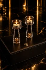 Lumière Gold Tealight Holders by GoldPrivé, two lit holders on a black leather box beside the emblem, flames above clear columns with gold sealed in their bases