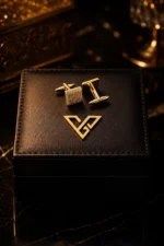 Axiom Gold Square Cufflinks by GoldPrive, a pair with finely knurled square faces on a black leather box beside the emblem