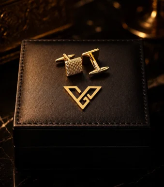 Axiom Gold Square Cufflinks by GoldPrive, a pair with finely knurled square faces on a black leather box beside the emblem